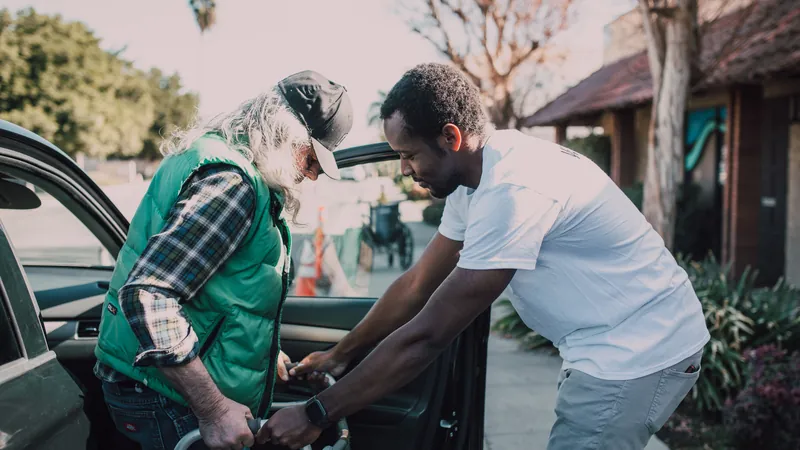 Caregiver assisting a senior with a walker into a vehicle for ambulatory medical transport